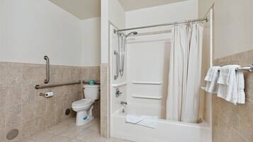 A bathroom with a bathtub, toilet, and handrails.