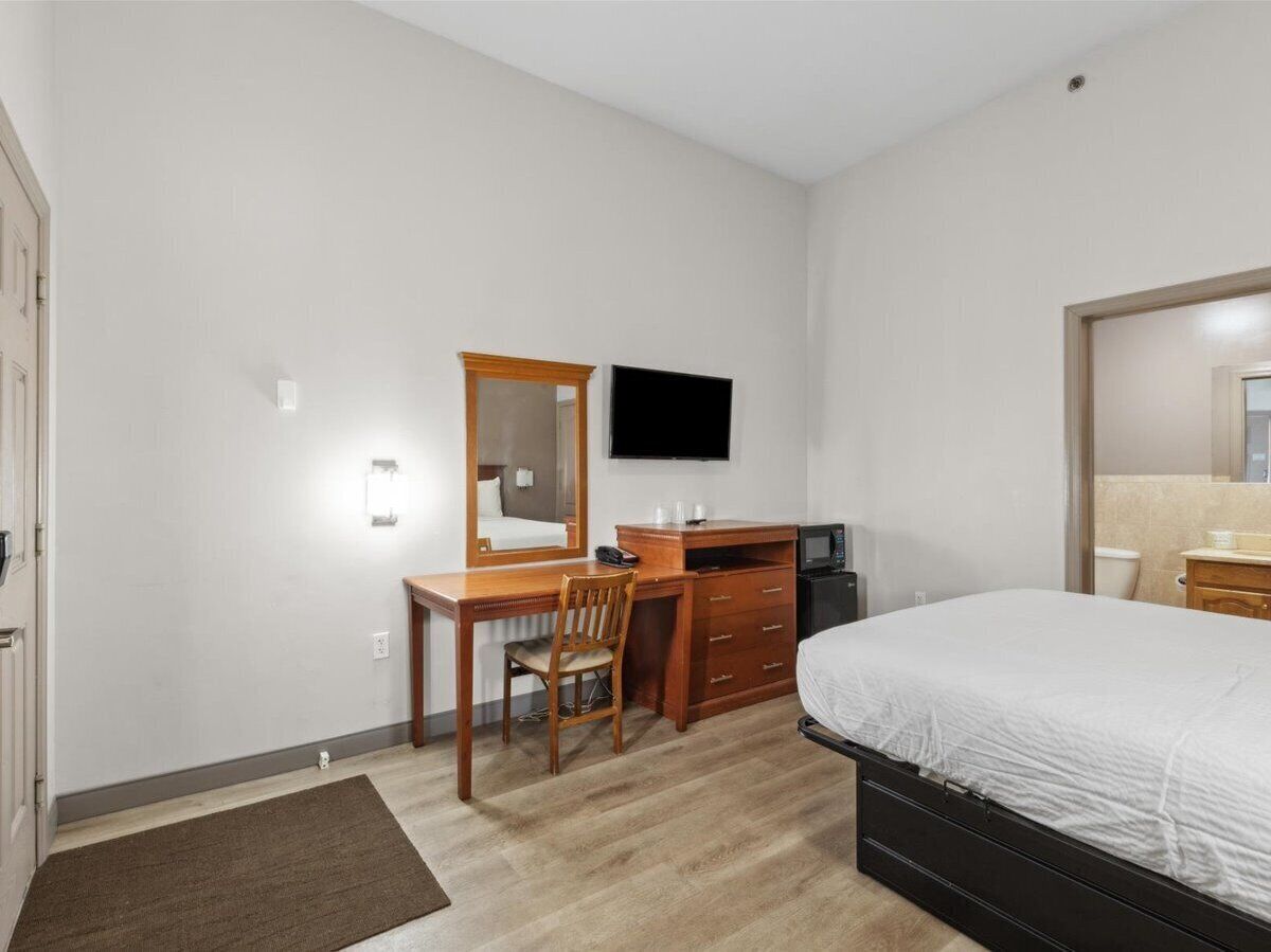 Une chambre d’hôtel comprenant un lit, un bureau avec une chaise, une télévision et une petite kitchenette.