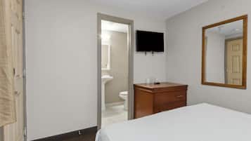 A hotel room with a bed, a wooden dresser, a television mounted on the wall, and a door leading to a bathroom.