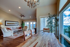 A spacious living room with a large wooden dining table, white sofas, and a view of the outdoors through large windows. - Beechin' Views (Beech Mountain)