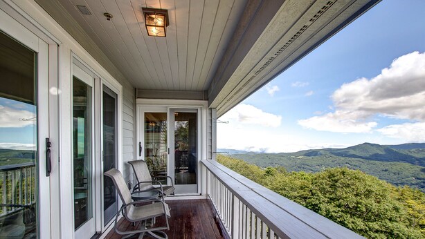 Un balcon doté d’une terrasse en bois, de balustrades blanches et offrant une vue sur un paysage montagneux.