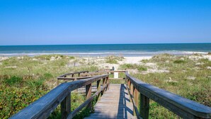 A wooden boardwalk leading to a beach with a clear view of the ocean.