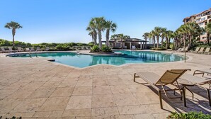 A swimming pool with lounge chairs and palm trees, surrounded by a building with multiple floors.