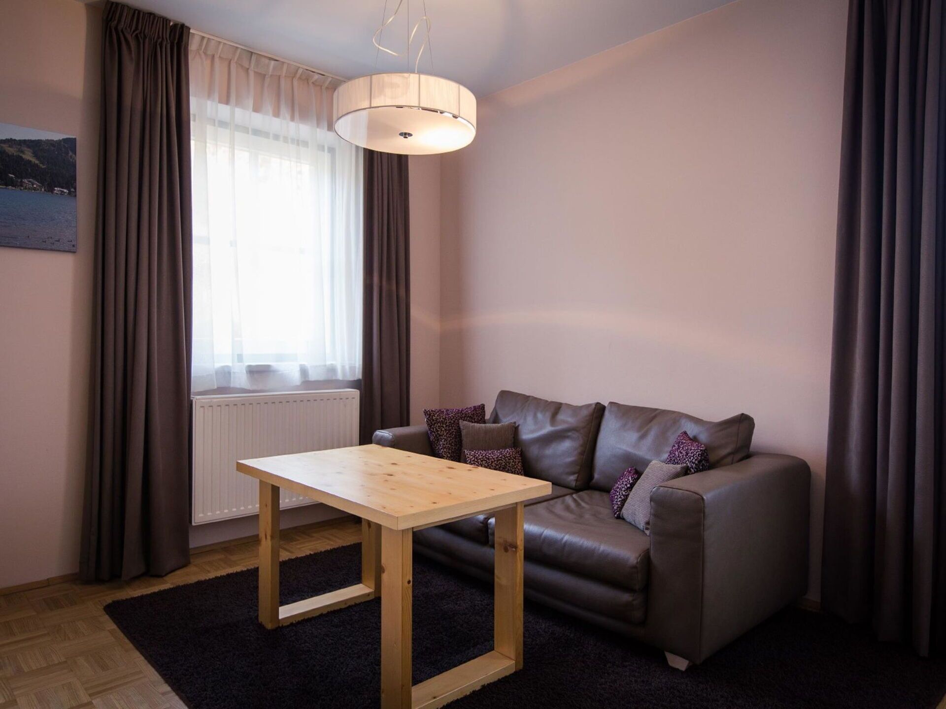 A modern living room with a leather sofa, a wooden coffee table, and a large window with curtains.
