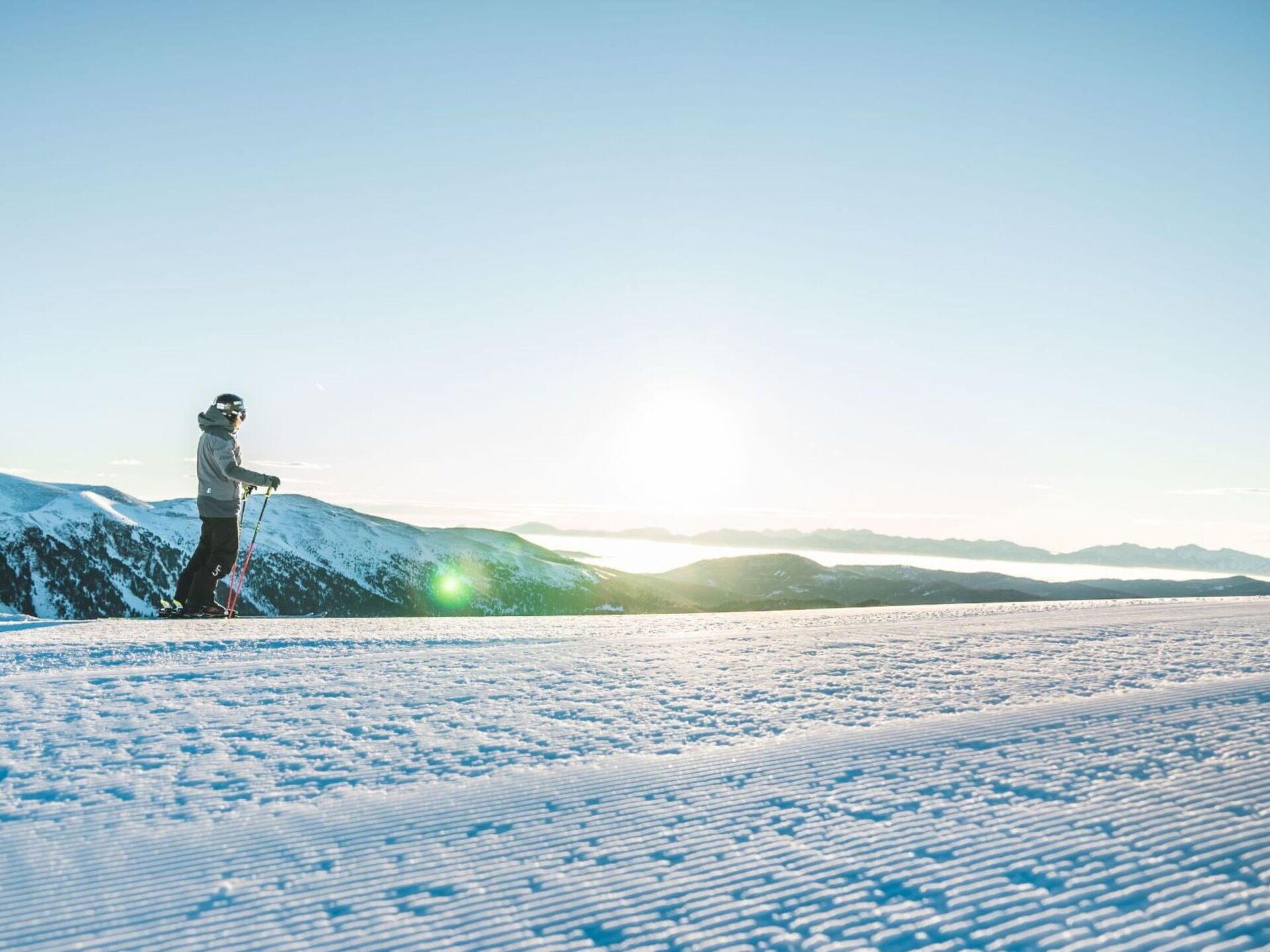 A person skiing on a snowy mountain slope with a clear sky and distant mountains.