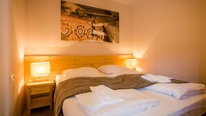 A hotel room with a wooden headboard, two bedside lamps, a bed with white linens and a striped blanket, and a wall-mounted artwork. - Nice apartment for 4 guests with WIFI, TV, balcony and panoramic view (Brandstätter)