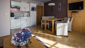 A modern kitchen with white cabinets, a microwave, and a coffee maker. There is a dining area with a wooden table and white chairs. A flat-screen TV is mounted on the wall. - Nice apartment for 4 guests with WIFI, TV, balcony and panoramic view (Brandstätter)