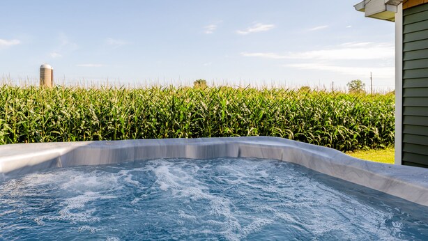 A hot tub with a view of a cornfield and a silo in the background.