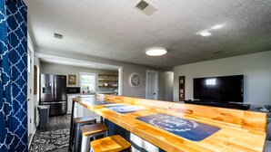 A modern kitchen with a wooden bar, bar stools, a refrigerator, microwave, and a TV.