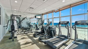 A gym with treadmills, elliptical machines, and weight equipment. Large windows offer a view of the beach. - Crystal Shores West 403 - BEACH FRONT | Zero Entry Pool, Indoor Pool, Hot Tub, Sauna, Fitness (Gulf Shores)