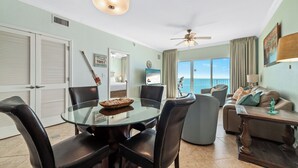 A spacious living area with a glass dining table, leather chairs, a sofa, and a view of the ocean. - Crystal Shores West 403 - BEACH FRONT | Zero Entry Pool, Indoor Pool, Hot Tub, Sauna, Fitness (Gulf Shores)