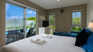Quarto de hotel com uma cama grande, televisão em uma mesinha, sofá e varanda com piscina.