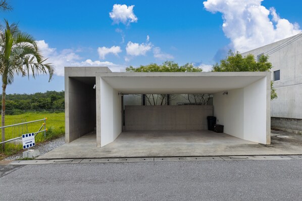 A modern building with a concrete facade, a covered entrance, and a palm tree nearby. - La Maison Blanche (Yomitan)