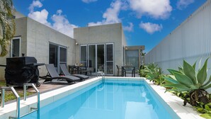 Uma área moderna ao ar livre com piscina, espreguiçadeiras, churrasqueira e plantas em vasos.