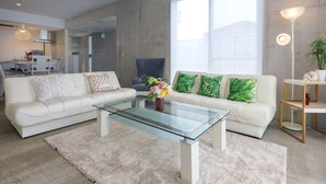 Uma sala de estar moderna com uma mesa de centro de vidro, sofás brancos e uma planta verde.