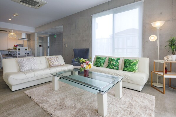 Una sala moderna con una mesa de centro de vidrio, sofás blancos y una planta verde.