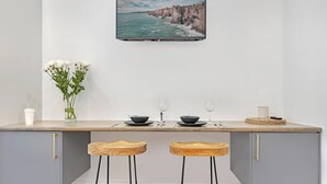 A modern kitchen with a large island, two wooden stools, a vase with flowers, and a framed coastal landscape picture above the island.