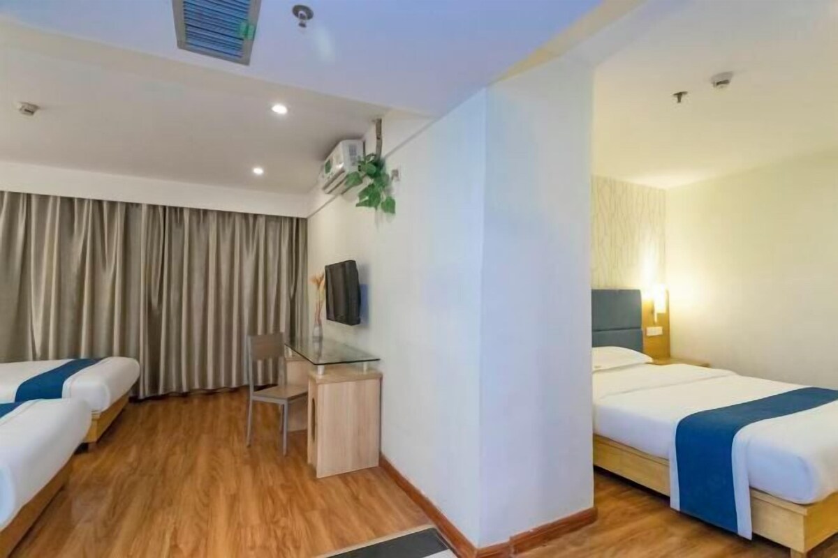 Habitación de hotel con dos camas, un escritorio, una silla, un televisor y una ventana con cortinas.