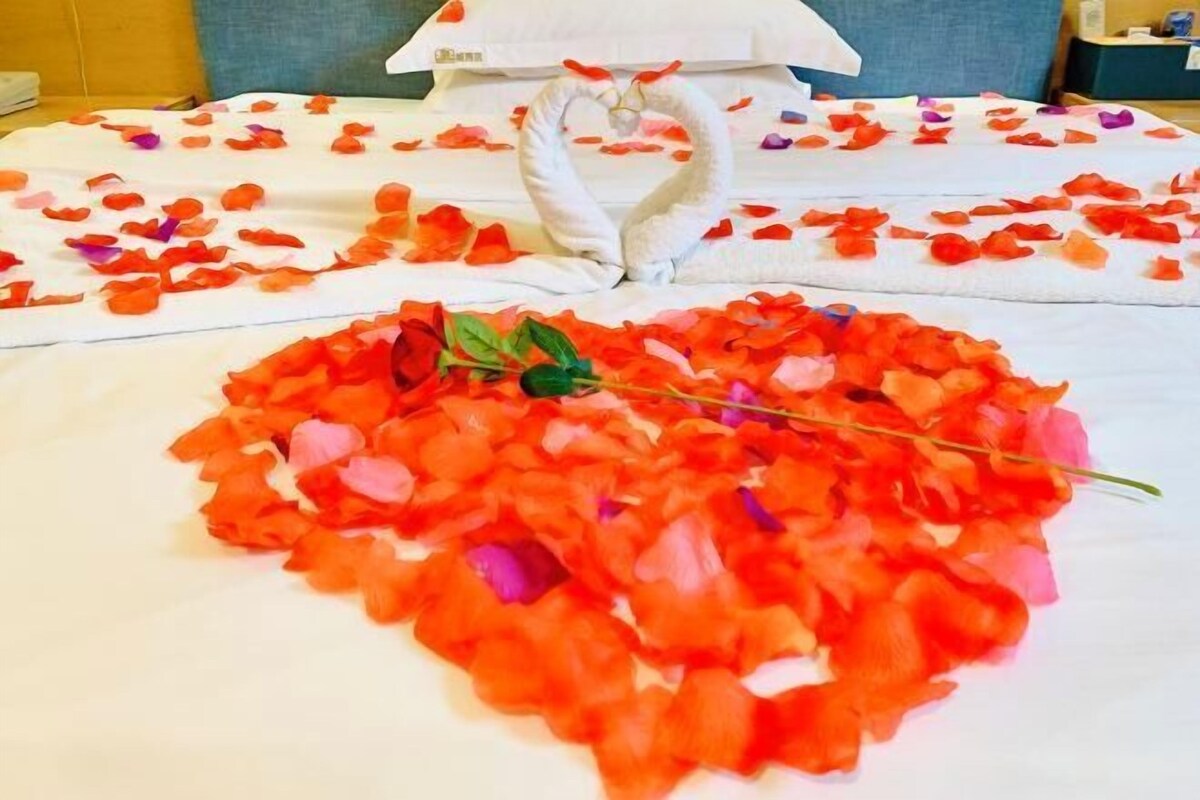 Una cama con pétalos de rosa y un cojín con forma de cisne.