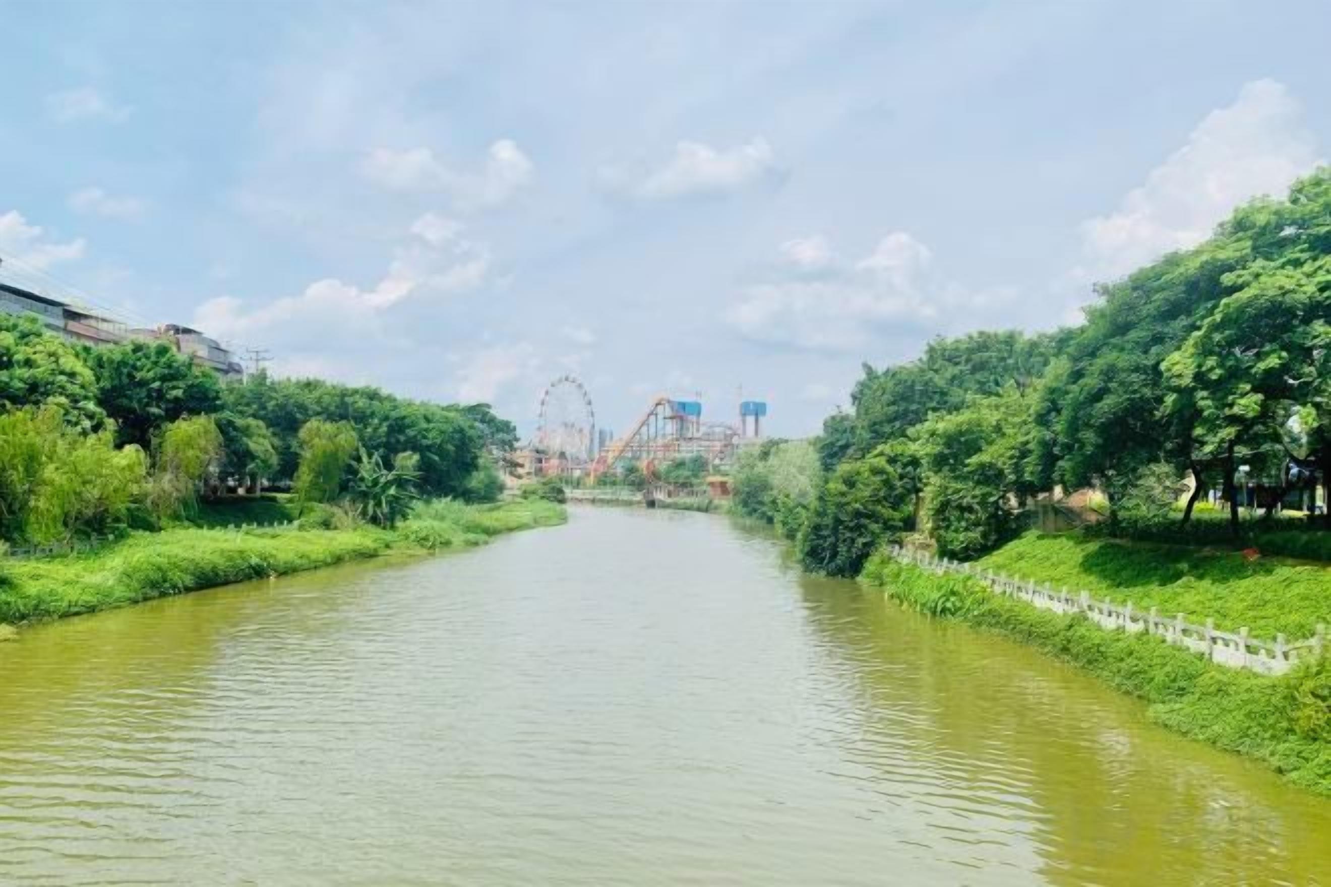 Un río con un puente, árboles y una noria a lo lejos.