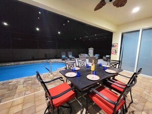 An outdoor pool area with a table set for dining, surrounded by chairs with red cushions.