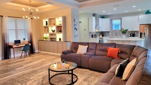 Ein modernes Wohnzimmer mit einer Eckcouch, einem Glastisch und einem Essbereich mit einer Küche im Hintergrund.