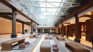 A spacious lobby with a high ceiling and a glass roof, featuring wooden benches and potted plants.