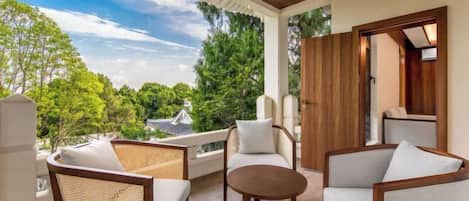 A balcony with wicker furniture and a round table, overlooking a lush green landscape.