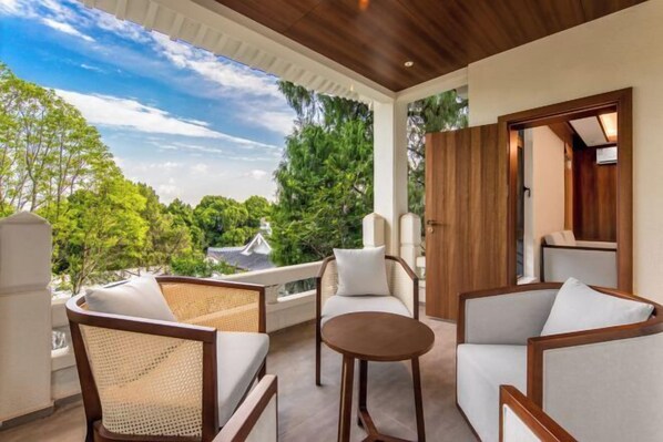 Un balcón con mobiliario de mimbre y una mesa redonda, con vistas a un paisaje verde y exuberante.