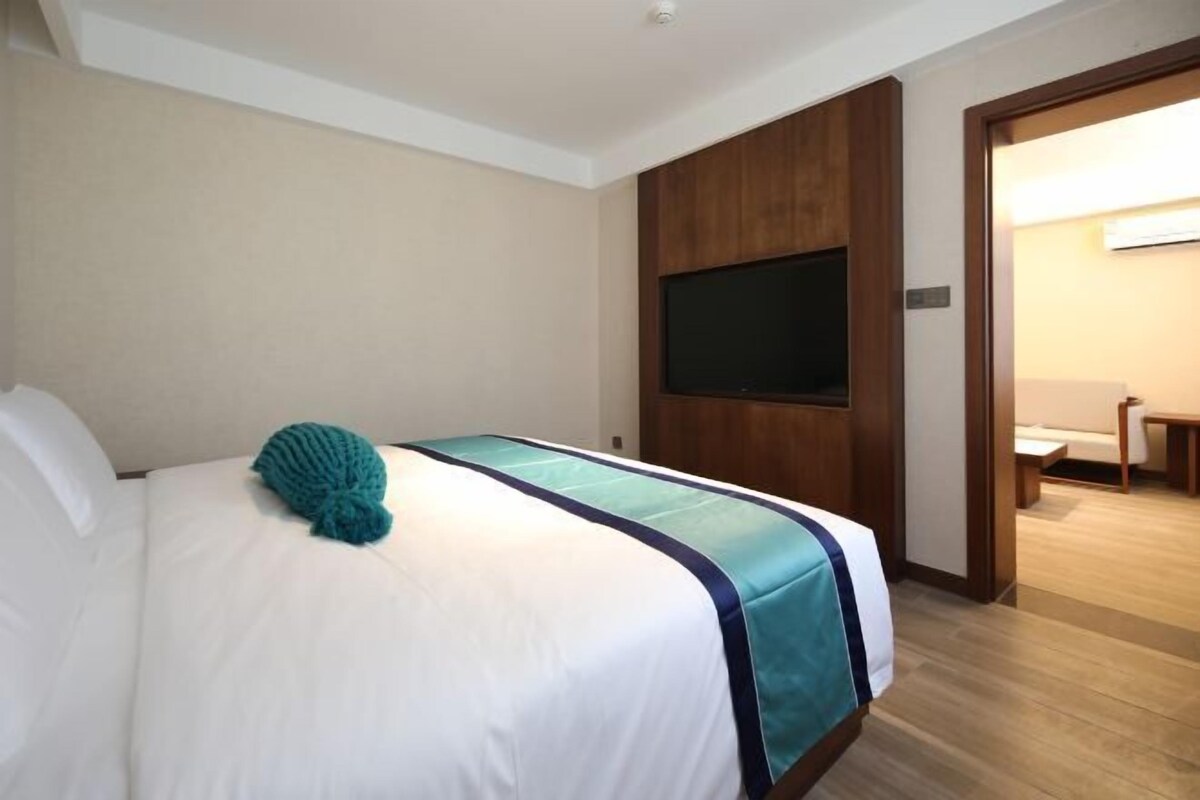 Una habitación de hotel con una cama, un televisor montado en la pared y una puerta de madera.
