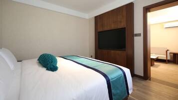 Quarto de hotel com uma cama, uma televisão fixada na parede e uma porta de madeira.