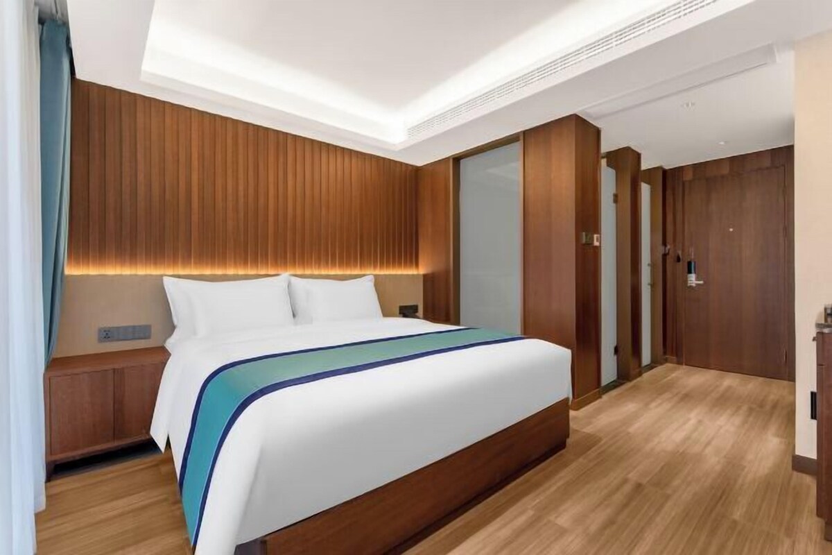 Una habitación de hotel moderna con una cama grande, paneles de madera en las paredes y suelo de madera.