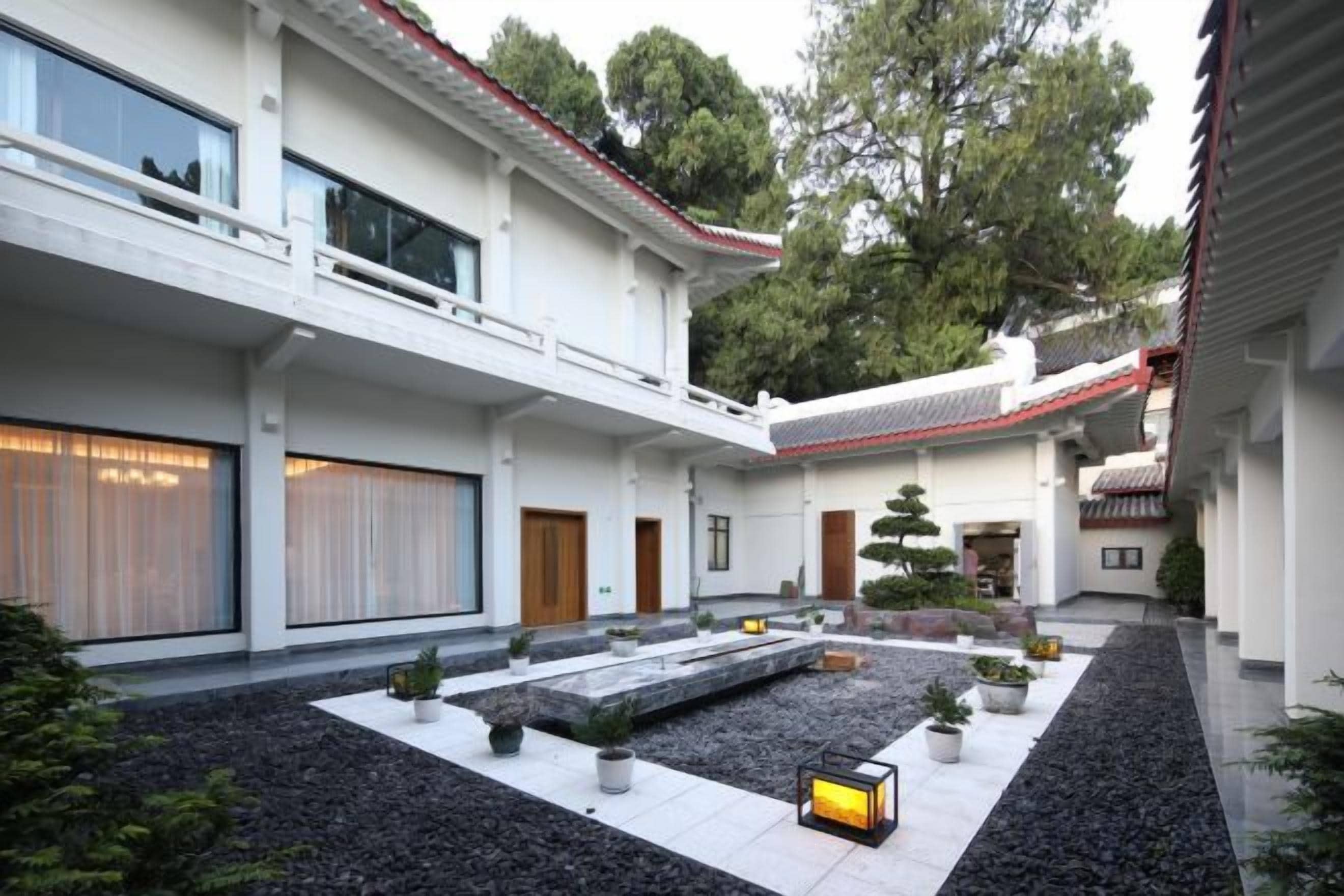 Un edificio moderno con un patio interior, que destaca por un techo tradicional, un estanque con carpas y plantas en macetas.