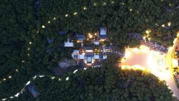 An aerial view of a property surrounded by dense forest, featuring multiple buildings and a well-lit driveway.