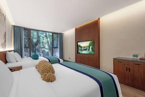 A hotel room with a large bed, a TV on the wall, a wooden cabinet, and a window with a view of trees.