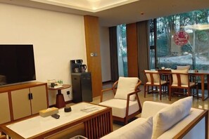 Una habitación de hotel moderna con una televisión grande, una cafetera, un sofá y una zona de comedor con sillas.
