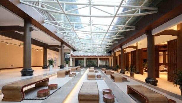 A spacious lobby with a high ceiling and a glass roof, featuring modern seating arrangements and a traditional architectural backdrop. - Qiqushan Hotel (Zitong)