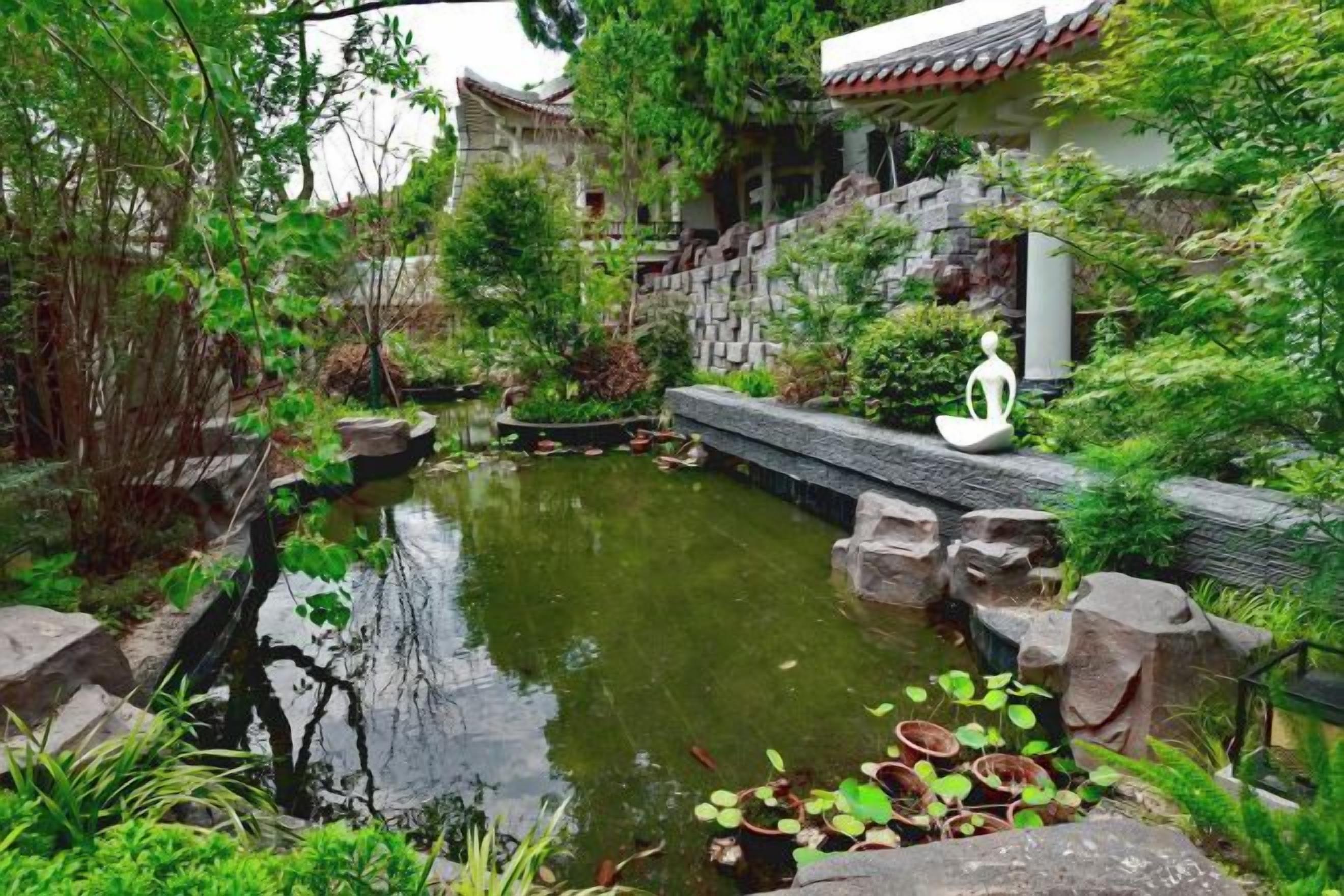 A traditional garden with a pond, stone pathway, and a building with a tiled roof.