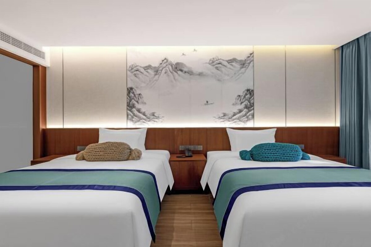 Habitación de hotel con dos camas, una obra de arte grande montada en la pared que muestra montañas y un cabecero de madera.