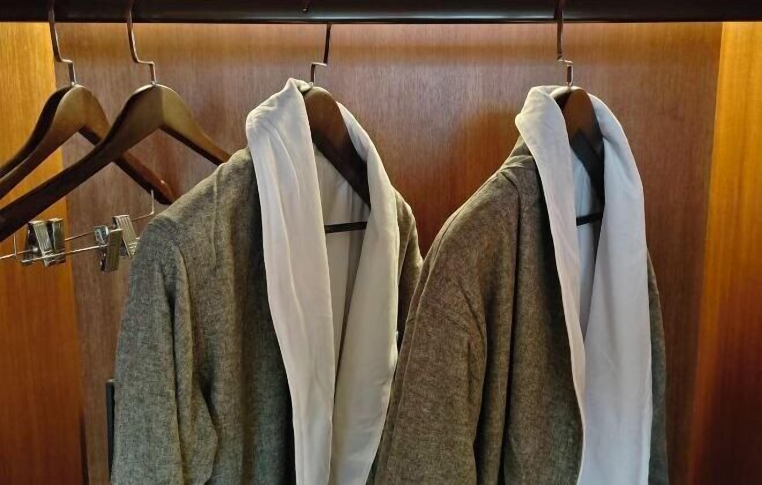 Un armario con perchas de madera que sostienen batas grises y blancas.