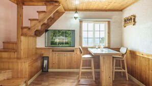 A wooden interior with a staircase, a dining area with a table and chairs, a television mounted on the wall, and a window with a view of greenery. - Ganghwa Gichayeohaeng Pension (Incheon)