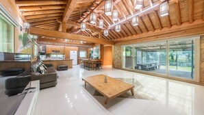 A spacious living area with a wooden ceiling, a kitchen area, and a large sliding glass door leading to an outdoor patio. - Ganghwa Gichayeohaeng Pension (Incheon)