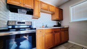 Una cocina con armarios de madera, estufa de acero inoxidable y salpicadero de azulejos blancos.