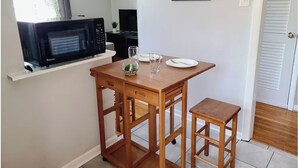 Una cocina compacta con microondas, una mesa de comedor con sillas y un ventanal con cortinas.