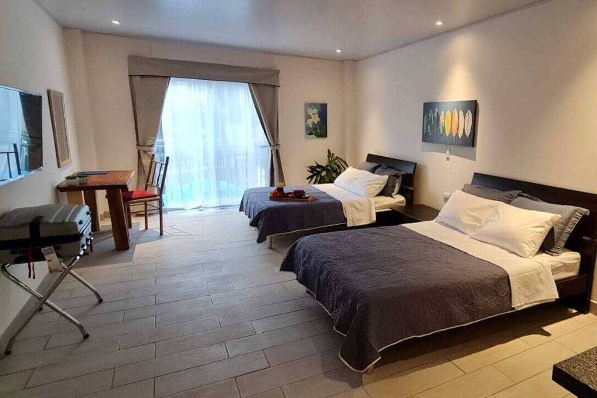 A hotel room with two beds, a desk, a chair, a TV, and artwork on the walls.