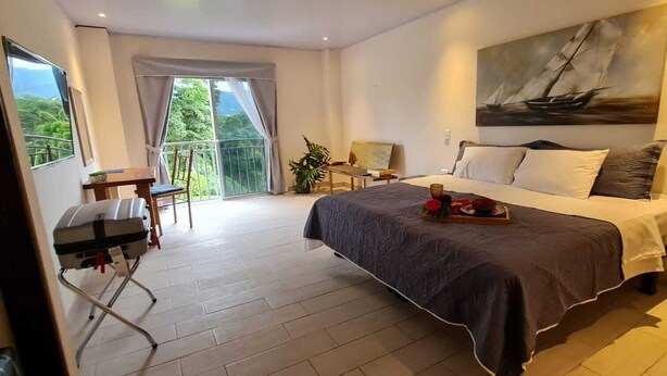 A hotel room with a bed, a desk, a chair, a balcony with a view, and a painting on the wall. - LOP Inn (La Asunción)