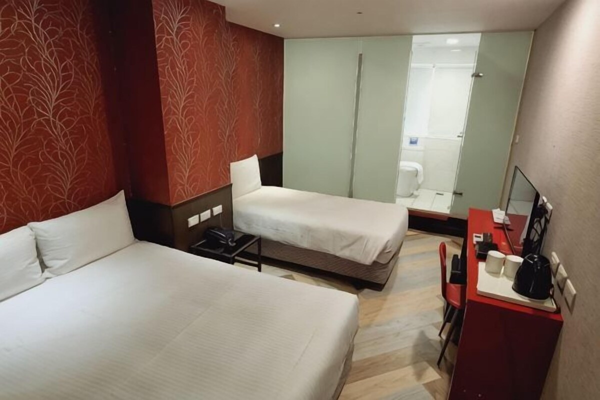 Hotelkamer met twee bedden, een bureau met stoel, een spiegel en een douche.