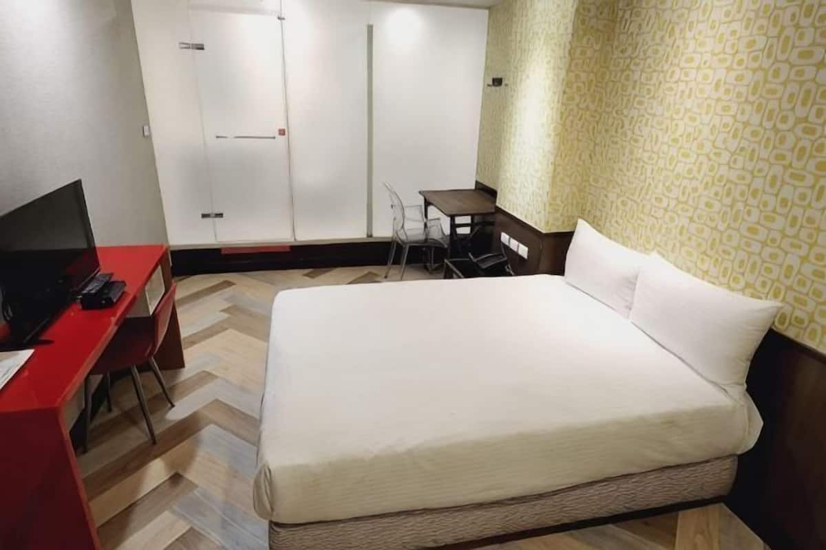 A hotel room with a bed, a desk with a computer, a chair, and a small table.
