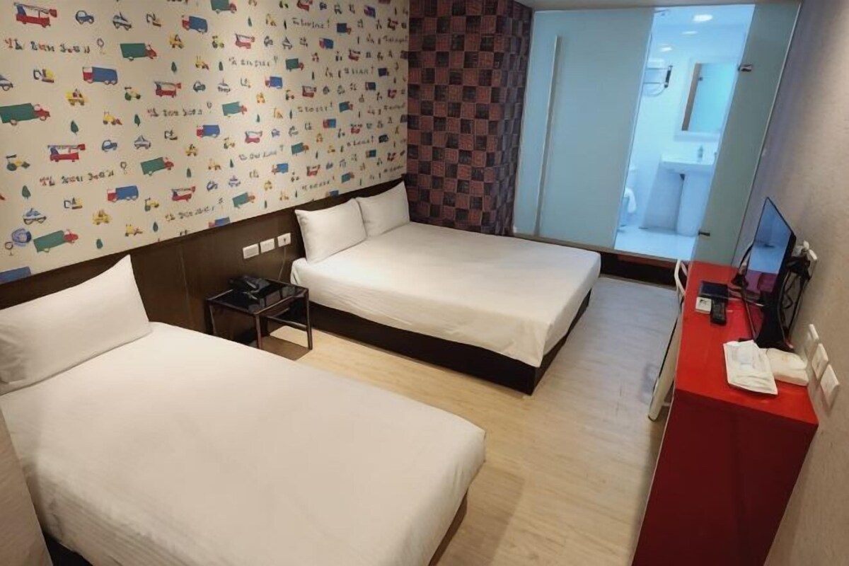 A hotel room with two beds, a small table, a red desk, and a wall with a patterned design.
