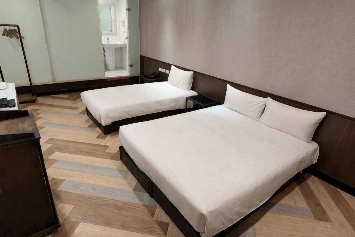 A hotel room with two beds, a desk, and a mirror.